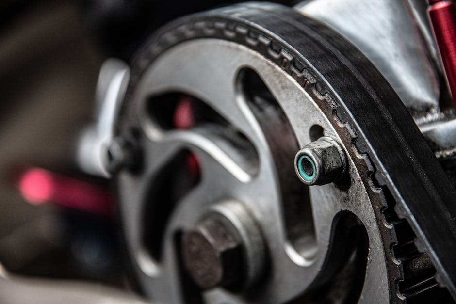 Closeup of black thin timing belt on round metallic camshaft sprocket in daylight on blurred background